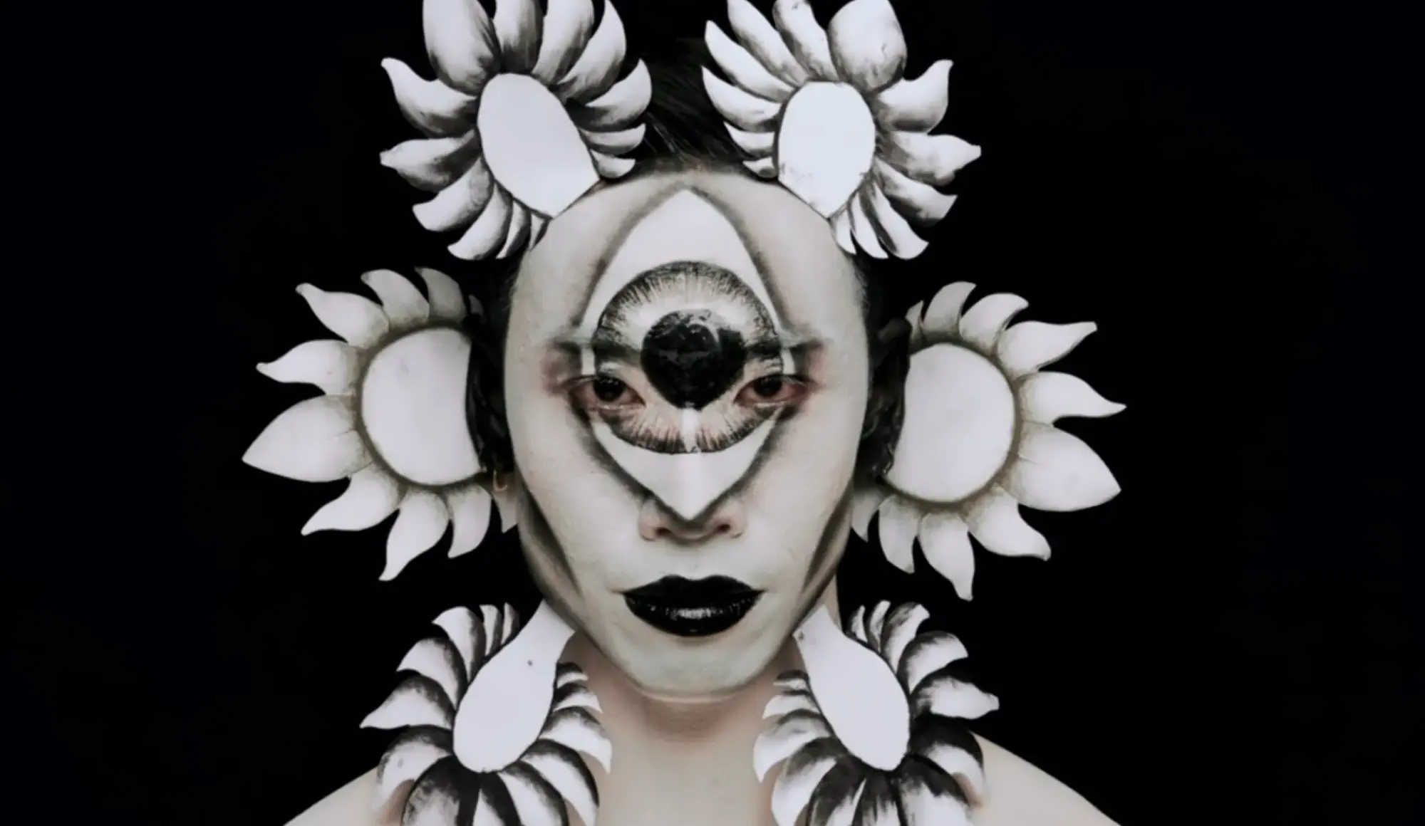 six petals surround a face painted black and white with a central eye motif